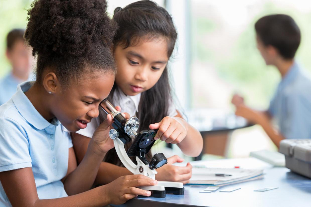 Two young girls take turns looking through microscope in science class. 