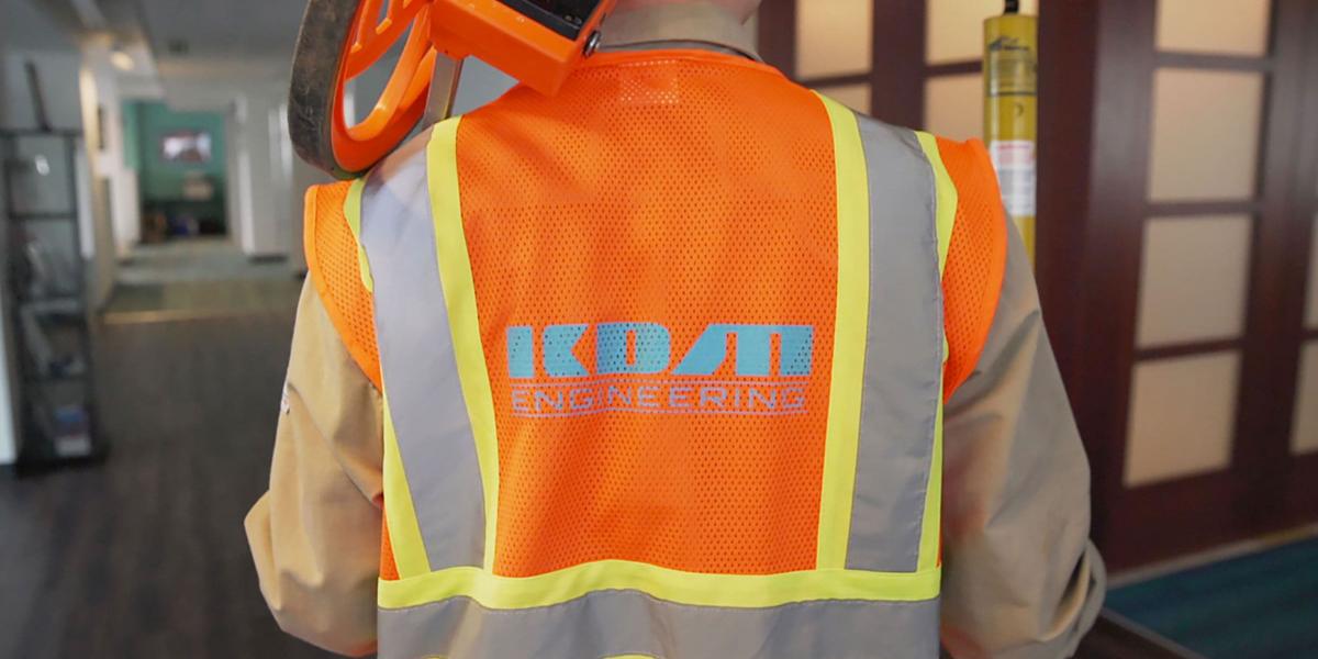 A KDM engineer poses with walk down engineering equipment in their company-issued PPE, including a safety vest with KDM logo